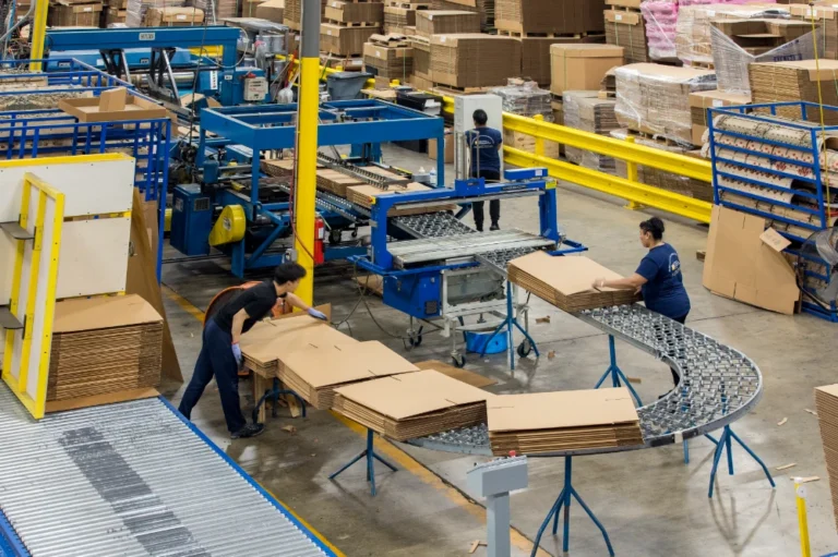 GPC workers are loading corrugated boxes onto a conveyor belt in the warehouse.